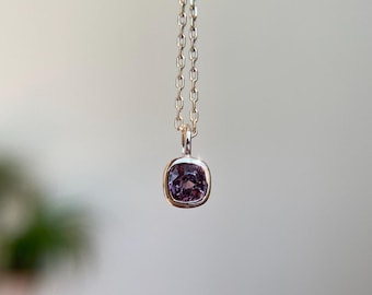 May include: A silver necklace featuring a square, purple gemstone pendant. The pendant is set in a silver bezel and suspended from a delicate chain. The gemstone has a faceted appearance.