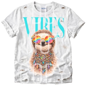 May include: White distressed t-shirt with a graphic of a sloth wearing rainbow sunglasses and a peace sign necklace. The word "VIBES" is printed in large, turquoise letters above the sloth.