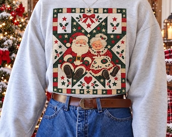 Puede incluir: Una sudadera gris claro de cuello redondo con un gran estampado gráfico rectangular que muestra a Santa Claus y la Señora Claus sentados juntos dentro de una estrella verde oscuro. El diseño incluye lazos rojos, hojas de acebo y pequeñas estrellas sobre un fondo crema.