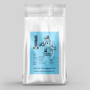 Peut inclure: Un sac blanc de café Espresso Vibe. Le sac présente une étiquette bleu clair avec le texte "Ethiopia Sidamo" et une illustration d'une personne préparant du café. L'étiquette comprend également le texte "Taste the Quality!" et "283g".