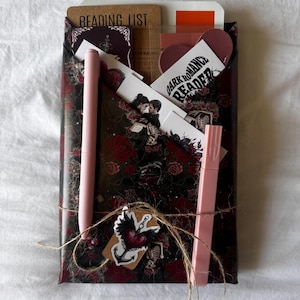 May include: A white ceramic mug with a black handle and the text "But First, Coffee" in a bold, black font. The mug is set against a blurred background, suggesting a cozy setting.