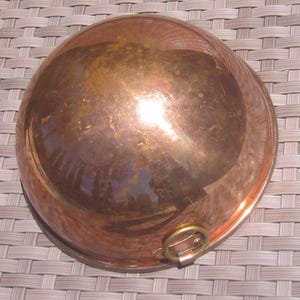 K&ouml;nnte beinhalten: Eine Kupfersch&uuml;ssel mit runder Form und einem kleinen Messinggriff. Die Sch&uuml;ssel hat eine polierte, reflektierende Oberfl&auml;che, die eine warme, r&ouml;tlich-braune Farbe aufweist. Die Sch&uuml;ssel wird wahrscheinlich zum Kochen oder zur Zubereitung von Speisen verwendet.