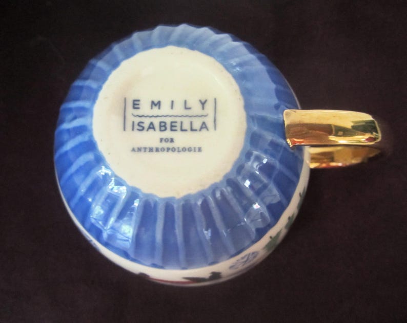 K&ouml;nnte beinhalten: Eine Keramik-Teetasse mit blau-wei&szlig;em Rippendesign. Der Griff ist goldfarben. Auf dem Boden der Tasse steht der Text "EMILY ISABELLA FOR ANTHROPOLOGIE".