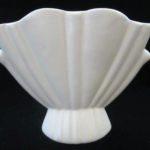 May include: A white ceramic vase with a fan-shaped design. The vase has a wide, open top and a narrow base.
