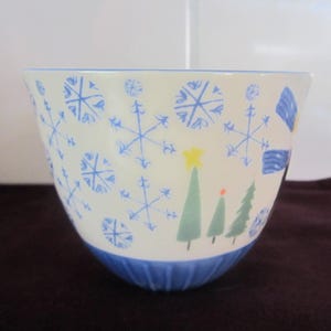 K&ouml;nnte beinhalten: Eine wei&szlig;e Keramiksch&uuml;ssel mit blauen Schneeflocken- und Weihnachtsbaum-Designs. Die Sch&uuml;ssel hat einen blauen Rand und Boden. Die Schneeflocken sind in verschiedenen Gr&ouml;&szlig;en und die B&auml;ume sind gr&uuml;n mit einem gelben Stern.