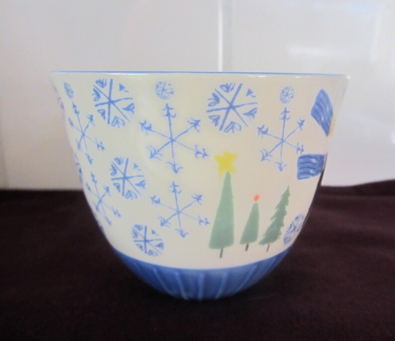 K&ouml;nnte beinhalten: Eine wei&szlig;e Keramiksch&uuml;ssel mit blauen Schneeflocken- und Weihnachtsbaum-Designs. Die Sch&uuml;ssel hat einen blauen Rand und Boden. Die Schneeflocken sind in verschiedenen Gr&ouml;&szlig;en und die B&auml;ume sind gr&uuml;n mit einem gelben Stern.