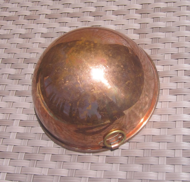 K&ouml;nnte beinhalten: Eine Kupfersch&uuml;ssel mit runder Form und einem kleinen Messinggriff. Die Sch&uuml;ssel hat eine polierte, reflektierende Oberfl&auml;che, die eine warme, r&ouml;tlich-braune Farbe aufweist. Die Sch&uuml;ssel wird wahrscheinlich zum Kochen oder zur Zubereitung von Speisen verwendet.
