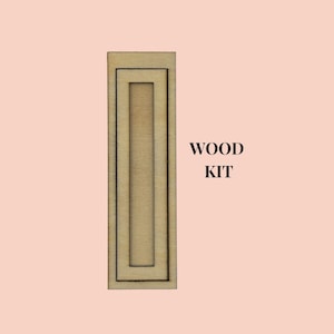 Peut inclure: Une découpe rectangulaire en bois de couleur claire présentant un design à cadre imbriqué avec une ouverture verticale centrale. L'objet est accompagné du texte noir WOOD KIT positionné à droite de la pièce en bois sur un fond pêche clair.