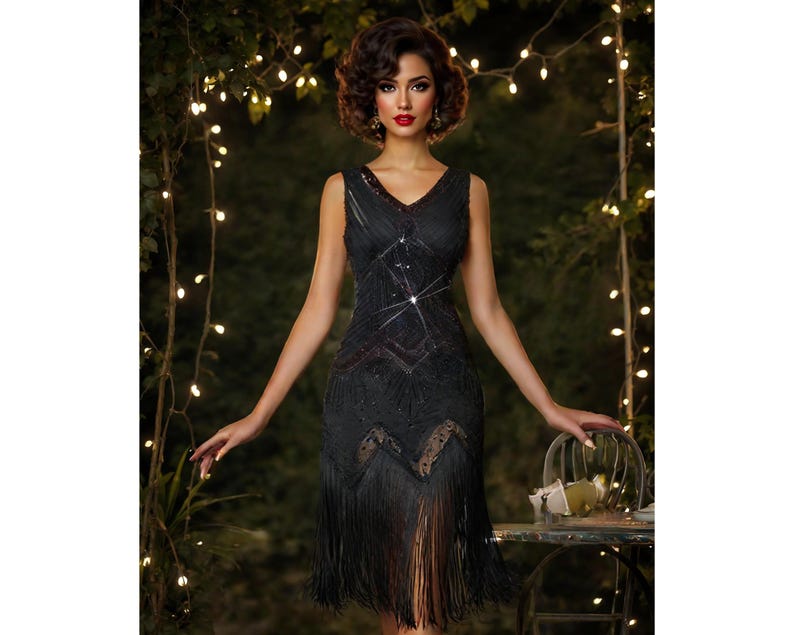 May include: A woman wearing a black sequined flapper dress with fringe. The dress has a V-neckline and is sleeveless. The woman is standing in front of a backdrop of greenery and lights.