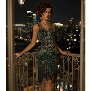 May include: A woman wearing a green and gold sequined flapper dress with fringe. The dress has a V-neckline and a fitted bodice. The woman is standing on a balcony with a city skyline in the background.