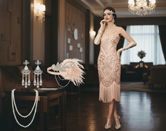 Op de afbeelding: Een vrouw in een perzikroze flapperjurk met franjes, lange handschoenen en een parelketting. Accessoires zijn een gevederde hoofdband en bungelende oorbellen. De setting is een kamer in vintage stijl met een kroonluchter.