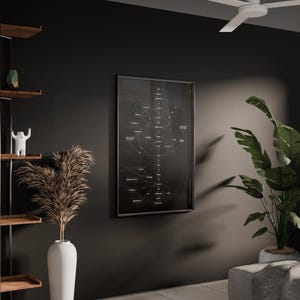 Puede incluir: Un marco en blanco y negro con un diagrama cuelga de una pared oscura. Un jarr&oacute;n alto y blanco contiene plantas secas. Una estanter&iacute;a de madera exhibe libros y objetos decorativos. Tambi&eacute;n se ven una gran planta en maceta y un sof&aacute; gris.