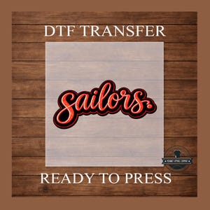May include: DTF transfer with the word "Sailors" in red script with a black outline. The text "DTF TRANSFER" and "READY TO PRESS" are above and below the design, respectively. The background is a wood grain pattern.