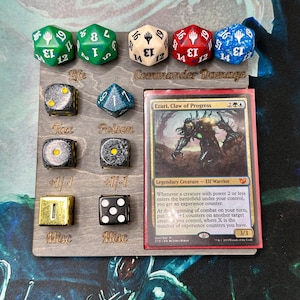 Może przedstawiać: Drewniana plansza do gry z kostkami i kartą. Plansza ma gniazda na kości z etykietami "Life", "Tax", "Poison" i "Misc". Sześć wielościennych kości w kolorze zielonym, białym, czerwonym i niebieskim znajduje się na górze. Karta Magic: The Gathering znajduje się po prawej stronie.