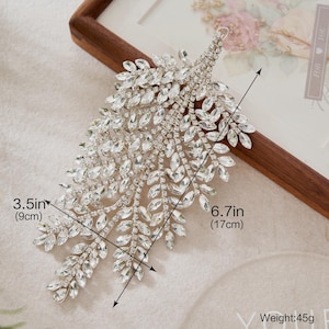 Puede incluir: Un accesorio para el cabello plateado en forma de hoja, de 17 cm de largo y 9 cm de ancho, adornado con numerosos cristales transparentes. La pieza pesa 45g. El diseño se asemeja a una rama estilizada, ideal para novias o eventos formales.