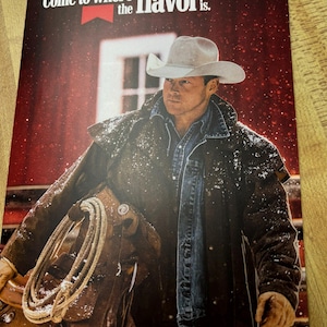 May include: A promotional image featuring a cowboy in a hat and a long coat, holding a saddle and rope. The text "Come to where the flavor is" is at the top. The background is a red barn.