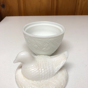 May include: A white ceramic dove-shaped trinket box with a matching lid. The lid is a dove sitting on a nest. The box has a textured, embossed design. The box is open, revealing the interior.