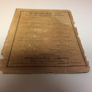 Puede incluir: Un anuncio antiguo de los remedios domésticos estándar de Spurlock-Neal Co. El papel envejecido tiene un tono marrón con texto negro que enumera varios remedios. El papel está rasgado en los bordes, mostrando su antigüedad. El texto incluye el nombre de la empresa y su ubicación en Nashville, Tennessee.