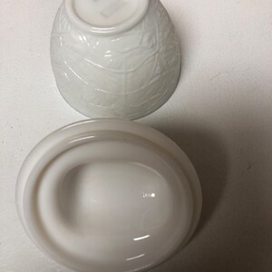 May include: A white, vintage-style bowl and lid set. The bowl has a textured leaf pattern, and the lid is oval-shaped with a handle. The set is made of opaque white glass.