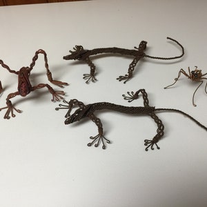 以下が含まれることがあります： 動物のワイヤースカルプチャー3点。茶色のカエル、茶色のトカゲ2匹、茶色のクモ。ワイヤーをねじって作られており、細部まで丁寧に作られています。