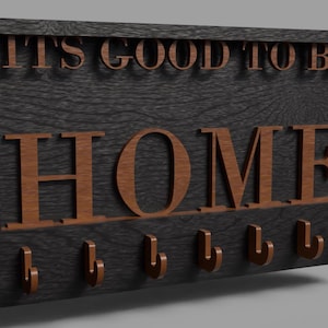 Può includere: Un porta chiavi in legno con il testo "It's good to be home" e sei ganci. Il porta chiavi è nero con lettere e ganci marroni.