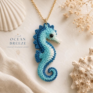 Könnte beinhalten: Eine Seepferdchen-Halskette mit einem Häkeldesign in Dunkelblau, Hellblau und Weiß. Das Seepferdchen hat ein kleines schwarzes Perlenauge und ist an einer goldfarbenen Kette befestigt. Der Text auf dem Bild lautet OCEAN BREEZE CROCHET SEAHORSE LOCKET.