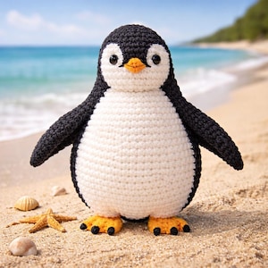 May include: A crocheted penguin toy on a sandy beach, with a starfish and seashells. The penguin has a black head, wings, and feet, with a white body. It has an orange beak and black eyes. The background shows the sea and sky.