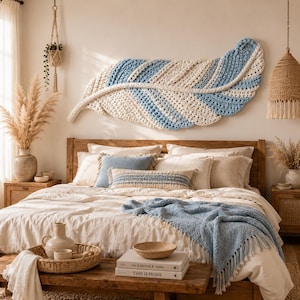 Pode incluir: Uma grande tape&ccedil;aria de parede em croch&ecirc; em forma de pena, feita com fio creme e azul claro. A pe&ccedil;a est&aacute; montada sobre uma cama com roupa de cama creme, uma manta azul e almofadas decorativas num quarto com m&oacute;veis de madeira.