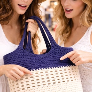 K&ouml;nnte beinhalten: Geh&auml;kelte Tragetasche in Marineblau und Creme. Der obere Teil ist marineblau, der untere Teil cremefarben mit einem Lochmuster. Die Tasche hat stabile marineblaue Griffe.