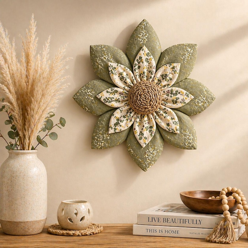 Puede incluir: Un gran adorno de pared con forma de flor de tela, con p&eacute;talos verde oliva y un centro con estampado floral. El centro es de material tejido. La flor est&aacute; montada en una pared beige.