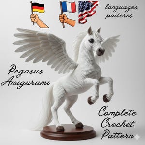 Può includere: Un amigurumi di Pegaso bianco all'uncinetto con grandi ali, in piedi su una base di legno. Il testo "Pegasus Amigurumi" e "Complete Crochet Pattern" sono visibili. L'immagine include anche le bandiere di Germania, Francia e Stati Uniti.