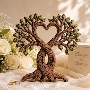 May include: A brown crocheted tree sculpture with intertwined trunks forming a heart shape. The tree has green leaves and the names "Sophia" and "Ethan" are written on the trunks. A box with "Forever & Always" is in the background.