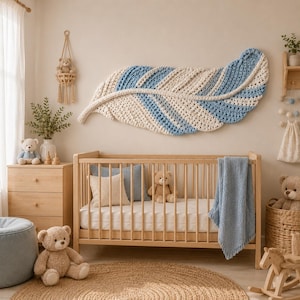 Pode incluir: Uma grande decora&ccedil;&atilde;o de parede em forma de pena de croch&ecirc; com listras alternadas de fio creme e azul claro. A pe&ccedil;a de arte t&ecirc;xtil possui uma espinha central e bordas texturizadas, exibida horizontalmente acima de um ber&ccedil;o de madeira.