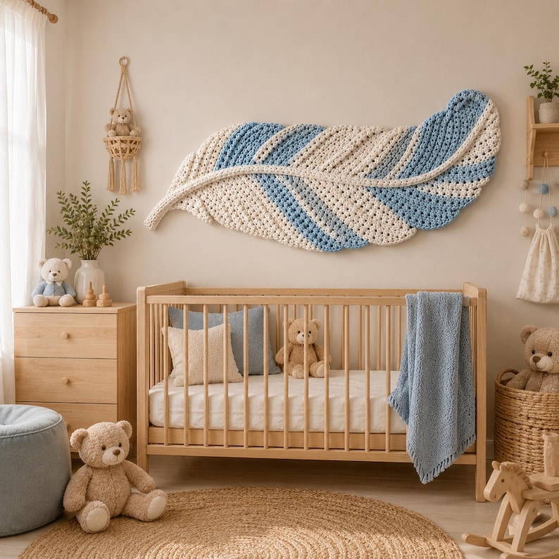 Pode incluir: Uma grande decora&ccedil;&atilde;o de parede em forma de pena de croch&ecirc; com listras alternadas de fio creme e azul claro. A pe&ccedil;a de arte t&ecirc;xtil possui uma espinha central e bordas texturizadas, exibida horizontalmente acima de um ber&ccedil;o de madeira.