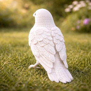 May include: A handcrafted, white crochet bird stands on green grass. The bird is detailed with textured feathers and a rounded body. The bird is a decorative item, possibly for home decor or a child's toy.