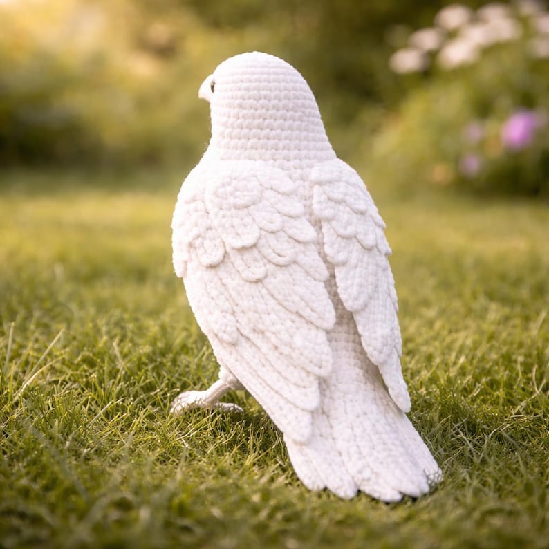 May include: A handcrafted, white crochet bird stands on green grass. The bird is detailed with textured feathers and a rounded body. The bird is a decorative item, possibly for home decor or a child's toy.