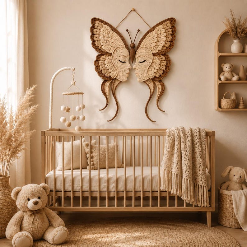 Peut inclure: Une grande d&eacute;coration murale en macram&eacute; repr&eacute;sentant un papillon avec deux visages sym&eacute;triques aux yeux ferm&eacute;s, dans des tons cr&egrave;me et marron. L'objet est plac&eacute; au-dessus d'un berceau en bois avec un mobile suspendu et un plaid textur&eacute;.