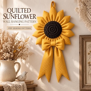 May include: A quilted sunflower wall hanging pattern featuring a dark brown center, yellow petals with a subtle grid texture, and a matching yellow bow with two long tails. The text reads QUILTED SUNFLOWER WALL HANGING PATTERN and PDF SEWING PATTERN.