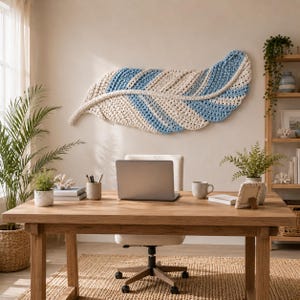 Pode incluir: Uma grande decora&ccedil;&atilde;o de parede horizontal em forma de pena, feita com fio grosso e texturizado em listras alternadas de creme e azul claro. A pe&ccedil;a apresenta uma nervura central e uma apar&ecirc;ncia tecida suave, montada numa parede lisa.