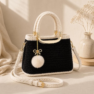 Peut inclure: Un sac à main en crochet noir et crème avec une poignée et une bandoulière crème. Le sac est orné d'éléments dorés et d'un charmant pompon crème. Un accessoire élégant.