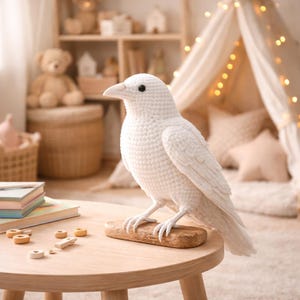May include: A handcrafted, white crochet raven figurine perched on a wooden base. The bird has a detailed, textured appearance with a realistic beak and black eyes. It is displayed on a small, round wooden table, suggesting a decorative or collectible item.