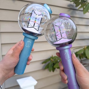 May include: Two light-up wands with clear globes and colorful handles. One wand is blue, the other is purple. Each globe has a geometric design and the word "you" in a cursive font. The handles have a logo.