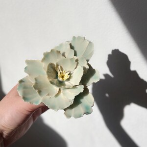 May include: A ceramic flower with a white and green glaze. The flower has a yellow center and is made to look like a peony.