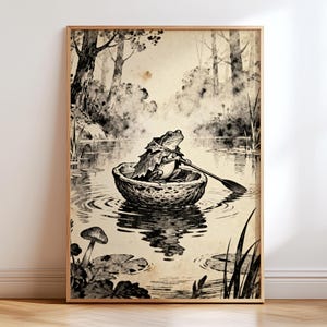 May include: A framed black and white illustration depicts a frog rowing a small boat on a lake. The artwork has a vintage aesthetic, with trees and foliage in the background. The frog is the focal point, holding an oar.