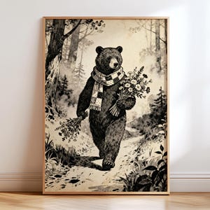 May include: A framed art print featuring a black and white illustration of a bear walking through a forest. The bear wears a scarf and carries a bouquet of flowers. The artwork has a vintage aesthetic, with a light brown wooden frame.