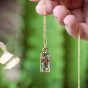 May include: A gold chain necklace with a rectangular pendant filled with colourful, iridescent, and sparkly stones.