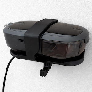 May include: A black and gray electric pencil sharpener mounted on a white wall. The sharpener has a clear compartment to view the shavings and a black power cord. A black strap secures the sharpener.