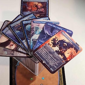 May include: A collection of Magic: The Gathering cards displayed on a Deckmaster card holder. The cards are all blue and feature various creatures and spells. The Deckmaster holder is brown with a blue border and the word "DECKMASTER" printed on it.