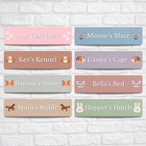 May include: A selection of rectangular signs in pastel shades, each with a pet's name and an animal illustration. The signs include names such as "Kev's Kennel," "Bella's Bed," and "Hopper's Hutch."