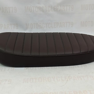 Peut inclure: Une selle de moto marron fonc&eacute; avec un design cousu et nervur&eacute;. La selle a une forme arrondie et est faite d'un mat&eacute;riau lisse. La selle est con&ccedil;ue pour une moto.